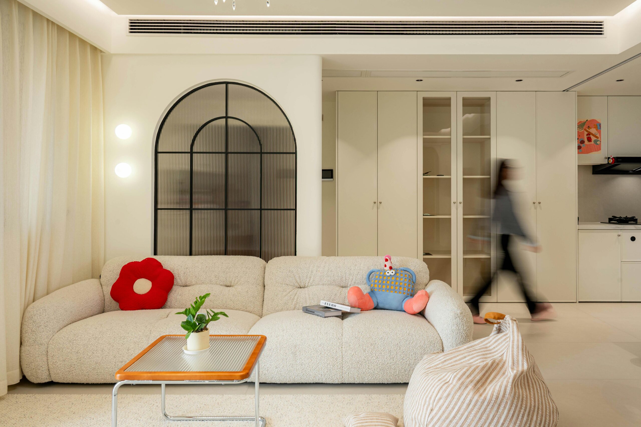 A modern living room featuring a plush sofa, abstract decorations, and a blurred person walking by.